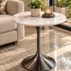 Modern round marble side table with dark graphite trumpet pedestal styled beside a beige sofa