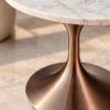 Close-up of brushed bronze tulip pedestal beneath white marble side table showing metallic texture and curved base