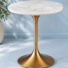 Gold finish tulip pedestal side table with round white marble top against a soft blue background