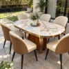 Luxury oval marble dining table with gold-finish edging and cream upholstered chairs in a sunlit garden-facing patio.