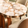 Close-up of white oval marble dining tabletop with gold and grey veining, rounded edge and gold-finish metallic trim.