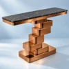 Sculptural black marble console table with offset copper-finish stainless steel blocks against a light blue studio background.