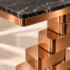 Close-up of black marble console tabletop with fine white veining, rounded corner and copper-tone stainless steel stepped base.