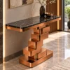 Designer black marble console table with sculptural copper-tone stainless steel pedestal in a contemporary hallway with wall art.