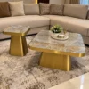 Gold stainless steel coffee table set with rectangular marble tops in front of a beige sectional sofa and patterned rug.