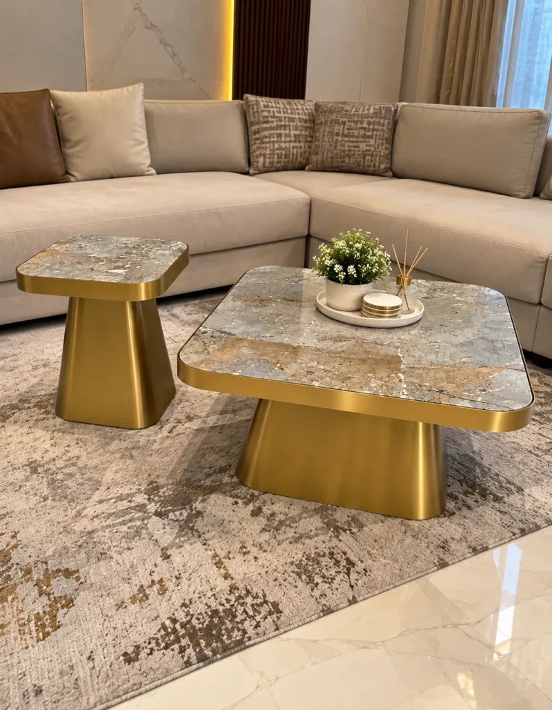 Gold stainless steel coffee table set with rectangular marble tops in front of a beige sectional sofa and patterned rug.