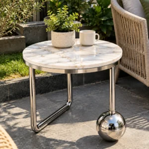 Round white marble side table with polished silver sphere base displayed beside patio lounge seating