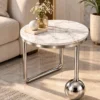 Luxury round marble side table with asymmetric steel support and polished metal ball base next to a sofa