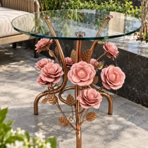 Round transparent glass side table with pink metal roses and bronze-gold floral legs in a sunlit seating area