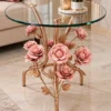 Rose gold floral side table with clear round glass top and sculpted pink flowers beside a luxury sofa