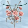 Silver chrome floral glass side table with pink rose decorations and three upward metal supports on blue background