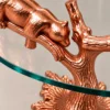 Close-up of resting bear sculpture and textured rose gold branches beneath round glass side table