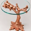 Rose gold sculptural tree branch side table with clear round glass top and resting bear detail from angled view