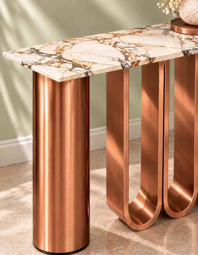 Close-up of white marble console tabletop with black and copper-toned veining beside cylindrical copper stainless steel and U-shaped loop supports.