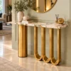 Modern gold and white marble console table with triple U-shaped base styled against a living room wall with round mirror.
