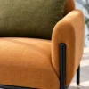 Close-up of caramel textured fabric accent chair showing curved padded armrest, olive-green cushion, stitched seat and black stainless steel frame.