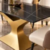 Close-up of polished black marble dining tabletop with fine gold and white veining above a sculptural gold stainless steel pedestal.