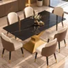 Elevated view of black marble dining table with gold sculptural base, five upholstered chairs and a decorative floral centrepiece.