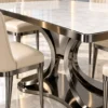 Close-up of white marble dining tabletop with rounded stainless steel edging and sculptural curved metallic pedestal.