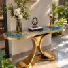 Luxury teal marble console table with gold curved dual-wing base and decorative flowers beside a sunlit garden entrance.