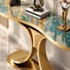 Close-up of teal marble console tabletop with cream and gold veining above a curved gold stainless steel dual-wing base.