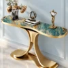 Modern teal marble console table with gold stainless steel curved base against a light blue wall with decorative sculptures.