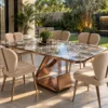 Modern marble dining table set with bronze-gold metal pedestal and cream chairs in a covered garden-facing dining area