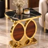 Designer gold marble side table with black rectangular top and sculptural dual oval base beside a cream sofa.
