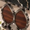 Close-up of black marble side table showing champagne graphite veining, polished metal frame and walnut-look oval support panels.