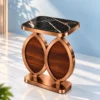 Modern antique coper side table with black marble top and two walnut-look oval supports displayed against a soft blue wall.